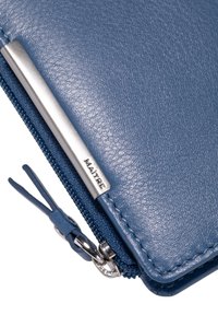 Portafoglio in pelle blu con superficie texturizzata, accessori in argento e chiusura con zip. Presenta una piccola linguetta con il nome del marchio "MAÎTRE."