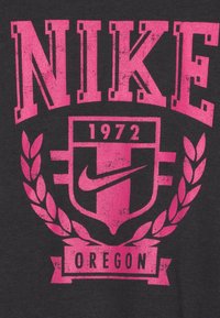 Camiseta negra con un gran logo rosa de Nike, el texto "1972" y "OREGON", junto con un gráfico de escudo y laurel. Presenta una textura desgastada.