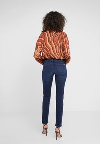 Blusa de manga larga de color óxido con rayas marrones onduladas, combinada con jeans ajustados de color azul oscuro y sandalias de tacón abierto.