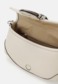Beige leather handbag with a smooth texture, featuring a zippered pocket inside, a magnetic snap closure, and brown accent details.