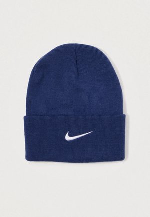 Tengerészkék kötött sapka puha anyagból, elöl fehér Nike logóval, hajtott szegéllyel a kényelmes illeszkedés érdekében.