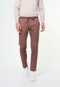 Pantalones de color marrón claro, con textura y cintura ajustable. Diseño entallado, combinados con zapatillas blancas y una camiseta de manga larga gris claro.
