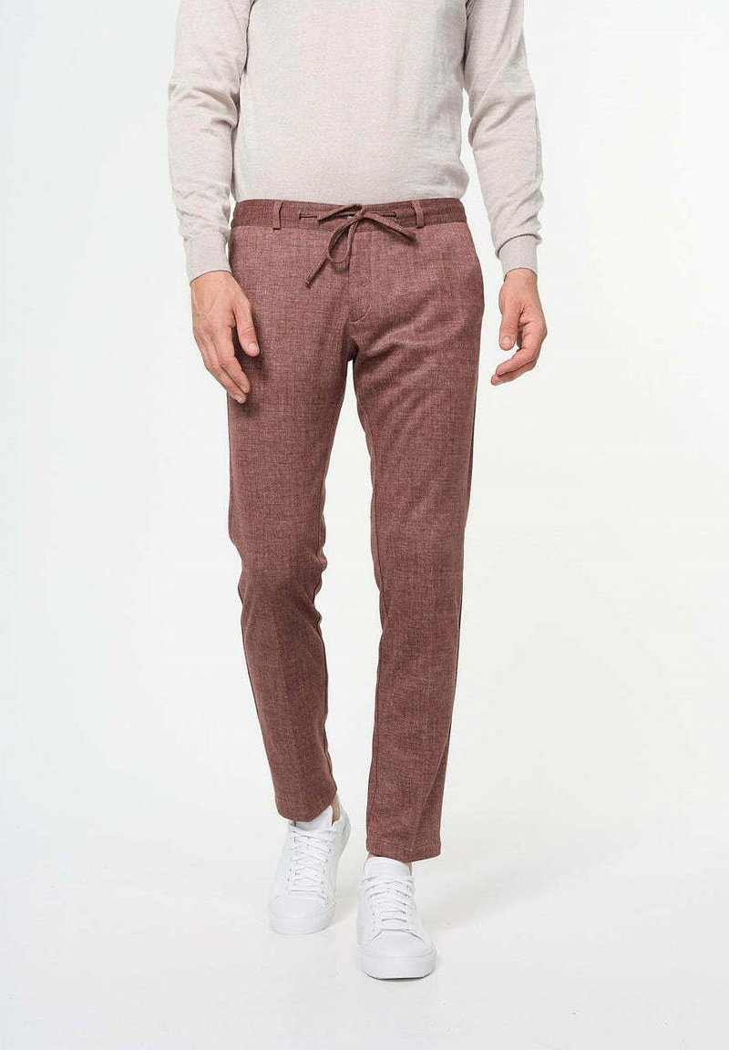 Pantalones de color marrón claro, con textura y cintura ajustable. Diseño entallado, combinados con zapatillas blancas y una camiseta de manga larga gris claro.