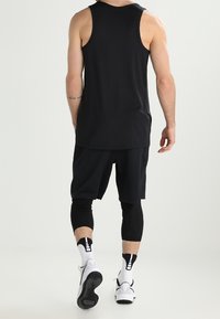 Canotta atletica nera senza maniche abbinata a pantaloni corti neri e leggings, accentuata da calze sportive bianche e sneakers.