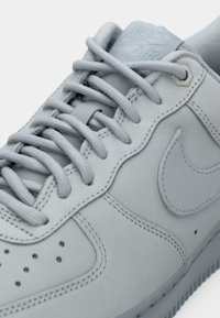 Gros plan d'une basket Nike Air gris clair montrant les lacets, les coutures, le logo de la marque brodé et les perforations sur le dessus du pied.