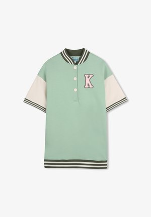 Polo en coton vert à manches courtes avec col côtelé, patte à trois boutons, manches crème et un "K" rose brodé sur la poitrine.