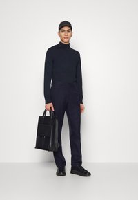 Mornarsko turtleneck pulover, prirejeni mornarski hlače, črne superge, črna kapa in črna usnjena nahrbtnik z sprednjim žepom.