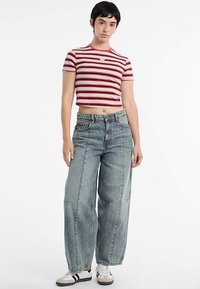 Top corto a righe rosse e bianche con maniche corte, abbinato a jeans larghi azzurri strappati e sneakers nere e bianche.