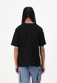 T-shirt nera in cotone con maniche corte e vestibilità rilassata, caratterizzata da un colletto a girocollo e una texture liscia. Indossata con pantaloni cargo azzurri chiari.