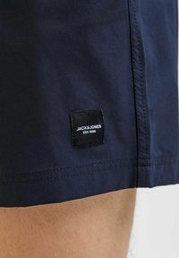 Sötétkék sort sima textúrával; a szegély közelében kis fekete címke található, fehér felirattal: "JACK & JONES EST. 1990".