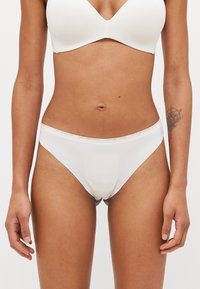 Balti medvilniniai bikini tipo apatiniai su lygiu paviršiumi, turintys logotipą akcentuojančią juostą ir be siūlių dizainą.