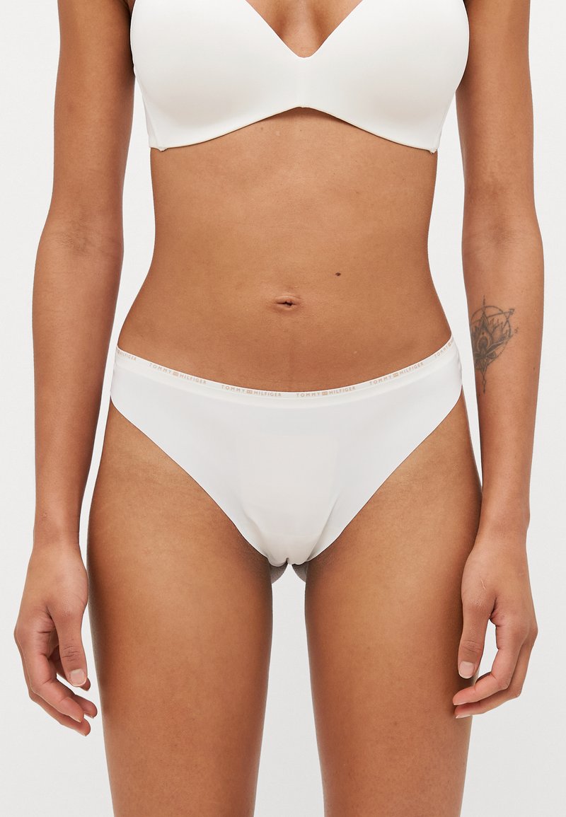 Balti medvilniniai bikini tipo apatiniai su lygiu paviršiumi, turintys logotipą akcentuojančią juostą ir be siūlių dizainą.
