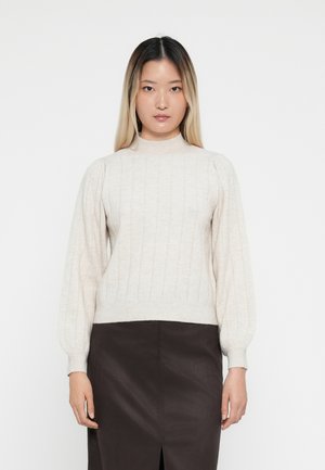 Maglione a coste beige chiaro con colletto alto, dotato di maniche a palloncino e orlo aderente, abbinato a una gonna marrone scuro.