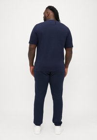 Mørkeblå t-skjorte med korte ermer og matchende bukser i mykt stoff, med klassisk passform. Brukt med hvite sneakers, sett bakfra.