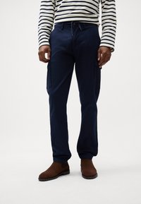 Marinblå cargo bukser med to sidelommer og slim fit, lavet af et holdbart stof. Parret med brune ankelstøvler og en stribet top.