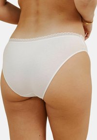Culotte en coton blanc avec une bordure en dentelle à la taille, présentant une texture lisse et une coupe couvrante. Pas de motifs visibles ni de matériel.