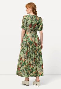 Maxikleid aus leichtem, grünem Stoff mit einem Dschungelmuster, das Elefanten, tropische Blätter und rote Akzente zeigt; kurze, puffige Ärmel.