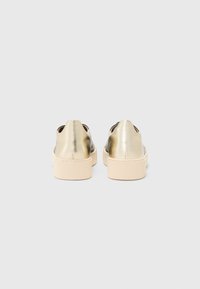 Metallic gold sneakers with a low-top design, featuring a thick beige rubber sole and a smooth texture, showing a minimalist style.