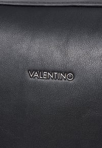 Melnas ādas rokassomu ar teksturētu virsmu. Iekļauts reljefs "VALENTINO" logo sudraba krāsā. Taisnstūra dizains ar minimālistiskiem akcentiem.