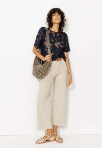 Haut en dentelle marine avec motif floral, pantalon large beige, sandales métalliques dorées, et sac à épaule en imprimé léopard.