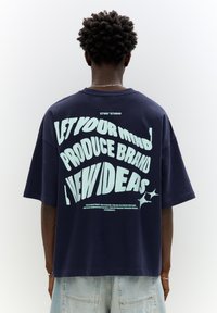Navy oversized t-shirt with light blue graphic text on the back. Cotton material with a relaxed fit and short sleeves, minimal stitching details.