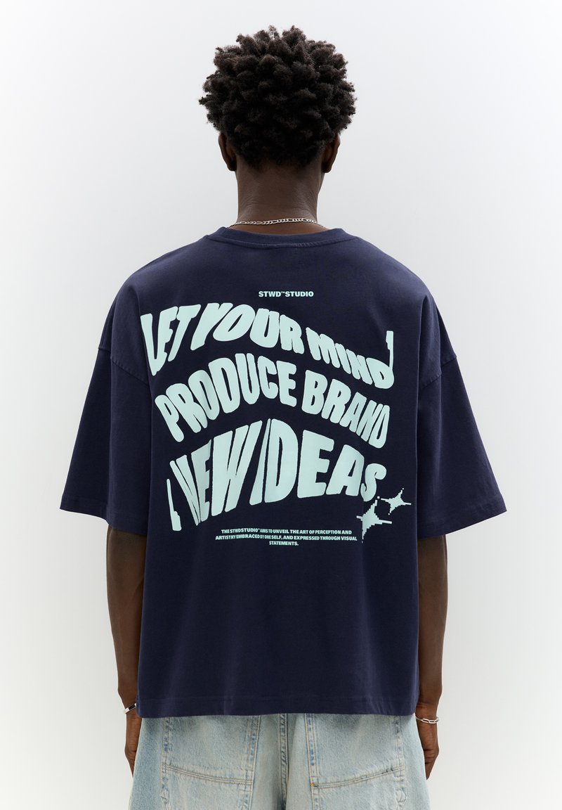 Navy oversized t-shirt with light blue graphic text on the back. Cotton material with a relaxed fit and short sleeves, minimal stitching details.