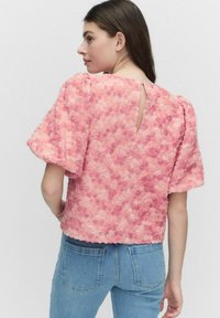 Kortärmad blus med en texturerad, lager-på-lager blommönster i nyanser av rosa, som har en nyckelhålsutskärning bak och en fyrkantig form.