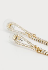 Boucles d'oreilles dorées au ton or, dotées d'un design incurvé, ornées de strass transparents. Des papillons transparents inclus pour un bon maintien.