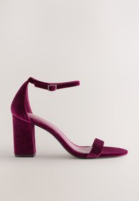 Fialový semišový sandál na vysokém podpatku s páskem kolem kotníku a blokovým podpatkem na světlém neutrálním pozadí.