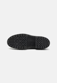 Semelle de chaussure noire en caoutchouc avec un motif texturé comportant des formes géométriques. Comprend des éléments de marque près du talon. Design durable pour une adhérence optimale.