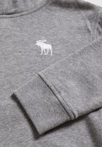 Grauer Baumwollpullover mit einem weißen, gestickten Elch auf der Brust und mit Bündchen versehenden Ärmeln. Weiche Textur mit einem lässigen Design.