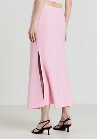 Rosa Maxiröcke aus weichem Stoff, mit einem seitlichen Schlitz, abschließendem Saum und einem taillierten Bund, kombiniert mit schwarzen Riemchenschuhen.