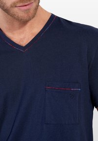 Mörkblå bomulls t-shirt med v-ringning, som har en kontrasterande röd och blå stickad kant samt en bröstficka med dekorativt kantband och logotyp.