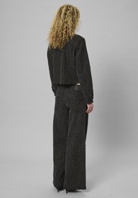 Czarna tweedowa kurtka o kroju cropped z luźnymi spodniami typu wide-leg, charakteryzującymi się teksturowanym materiałem i błyszczącymi srebrnymi akcentami. Gładkie skórzane detale.