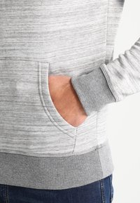 Sudadera gris con un dobladillo y puños acanalados y texturizados. Cuenta con un bolsillo delantero y una tela suave y mezcla. Diseño casual con detalles en contraste.