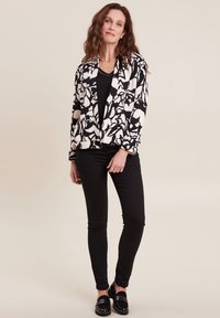 Schwarze und weiße Blazer mit Blumenmuster, lange Ärmel, offener Front, kombiniert mit einem schwarzen Oberteil und schmal geschnittenen schwarzen Hosen. Schwarze Loafers runden das Outfit ab.
