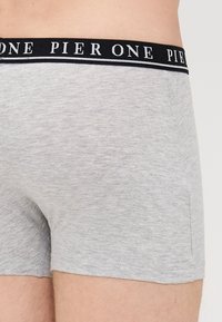 Boxeri din bumbac gri cu un elastic negru pe care este inscripționat textul "PIER ONE." Textură netedă și design ajustat, cu detaliu de buzunar lateral.