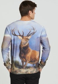 Sudadera de manga larga con un gráfico detallado de un ciervo en colores apagados, diseño en degradado que pasa de azules a tonos terrosos, textura de tela suave.