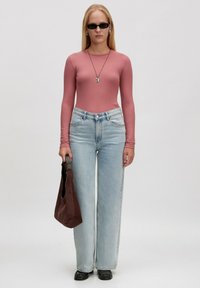 Langärmliges, geripptes pinkes Oberteil, hellblaue, hochgezogene Jeans, schwarze Sonnenbrille, silberne Halskette, braune Wildledertasche, schwarze Schuhe, minimalistisches Design.