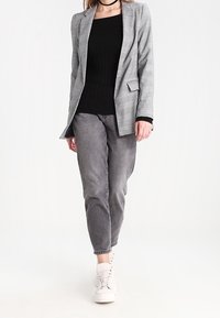 Grauer karierten Blazer über einem schwarzen, gerippten Oberteil, kombiniert mit grauer Jeans und weißen Sneakers. Das Outfit zeichnet sich durch eine maßgeschneiderte Gestaltung und eine legere Passform aus.