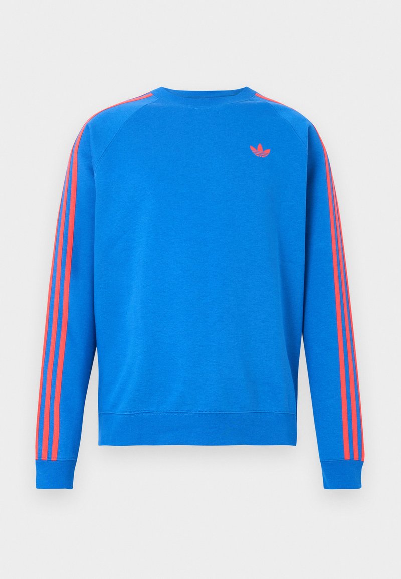 Sweat-shirt bleu avec un col rond côtelé, des rayures rouges en accent sur les épaules et un petit logo sur la poitrine. Texture de tissu douce.