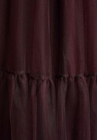 Ciemne bordowe warstwowe tiulowe tkaniny o drobnej siateczkowej strukturze i marszczeniach tworzących miękkie pionowe fałdy.