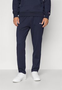 Navy Sweatpants aus weichem Material mit einem elastischen Bund und dezentem Logo an der Seite; kombiniert mit weißen Sneakers.