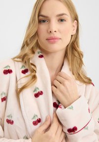Albornoz de forro polar con una tela suave de color rosa pálido que presenta un patrón de cerezas. El diseño incluye cerezas rojas y hojas verdes, con detalles de cinta en las mangas.