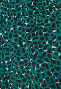 Tissu turquoise avec une surface texturée, arborant un motif léopard noir et blanc, accentué de taches bleues sur toute la surface.