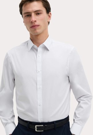 Biała, długosleeve, zapinana na guziki koszula z klasycznym kołnierzykiem, wykonana z gładkiego materiału, w slim fit i z białymi guzikami, noszona z czarnym paskiem.