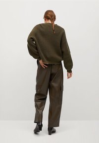 Przesadny oliwkowo-zielony sweter z dzianiny o teksturowanym wzorze, zestawiony z luźnymi brązowymi spodniami cargo z sztucznej skóry i czarnymi botkami za kostkę.