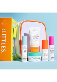 Set de soins Drunk Elephant avec nettoyant, sérums, crème, emballage coloré et une trousse de voyage blanche zippée avec bordure orange.