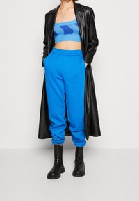 Modrý cropped pletený top s vlnkovým vzorem spárovaný s modrými tepláky. Pohodlně zkombinován s dlouhým černým koženým kabátem a černými botami s robustní podrážkou.