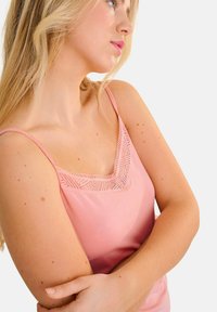 Camisole rose pâle avec une bordure en dentelle et des motifs géométriques le long de l'encolure. Bretelles fines ajustables et coupe décontractée.